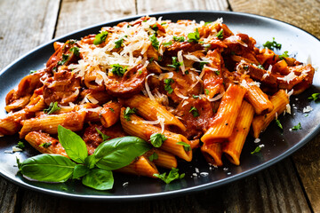 Penne with sausages, tomato sauce, parmesan cheese, basil and vegetables served on wooden table