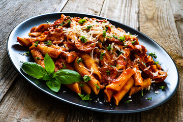 Penne with sausages, tomato sauce, parmesan cheese, basil and vegetables served on wooden table