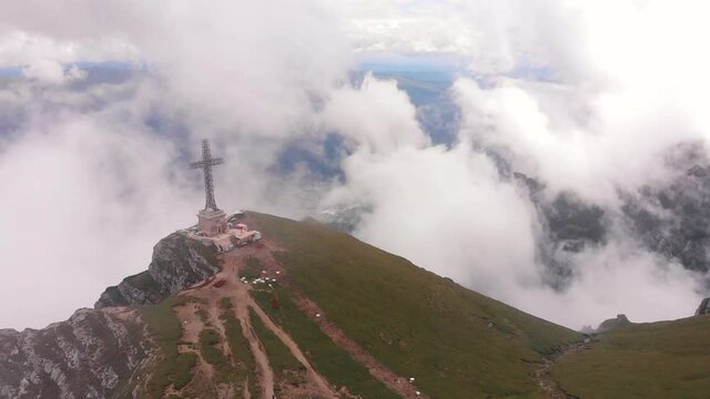Aerial drone flight over Caraiman Heroes' Cross in Bucegi mountains, Romania, with sea of clouds above Busteni town in Prahova Valley