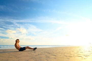 Fototapeta na wymiar Sports and healthy lifestyle. Young man doing crunches on the ocean beach.