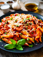 Penne with sausages, tomato sauce, parmesan cheese, basil and vegetables served on wooden table