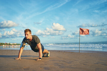 Sports and healthy lifestyle. Young man doing push-ups on the ocean beach.