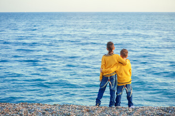 boys standing on a beach holding hands, view from the back