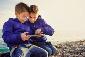 brothers, playing together with tablet pc sitting outdoors