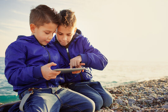 brothers, playing together with tablet pc sitting outdoors