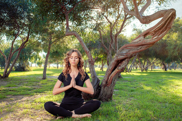 Young woman with closed eyes in lotus pose in the park