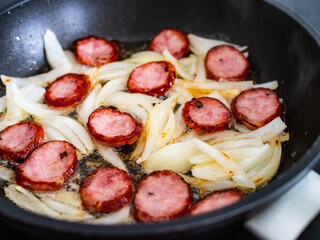 Frying sausage slices and white onion in pan
