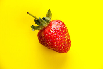 Bright red strawberry on a yellow background close-up.