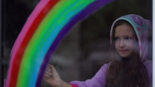 Stay home, flash mob chase the rainbow. girl in pajamas draws the rainbow on the window at home.