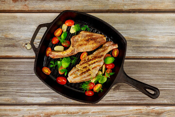 Grilled pork steak in iron skillet on wooden background.