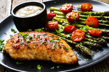 Tasty roast chicken breast, green asparagus, cherry tomatoes  and garlic dip on wooden table
