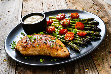 Tasty roast chicken breast, green asparagus, cherry tomatoes  and garlic dip on wooden table
