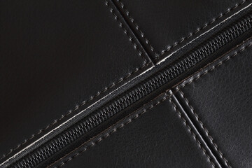 Black leather background with seams and a plastic zipper. Leather bag element. Closeup