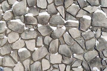 Snowy stone wall texture. Cement wall decorated by large gray flat cobble stones and partially covered by snow. Building facade decoration for winter background