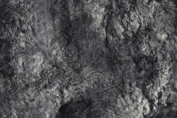 Texture of natural sheepskin. Worn uneven gray fur background. Bumpy surface of a used lambskin material. Top view. Closeup