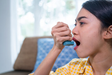 Asian woman having an asthma attack using an asthma inhaler at home