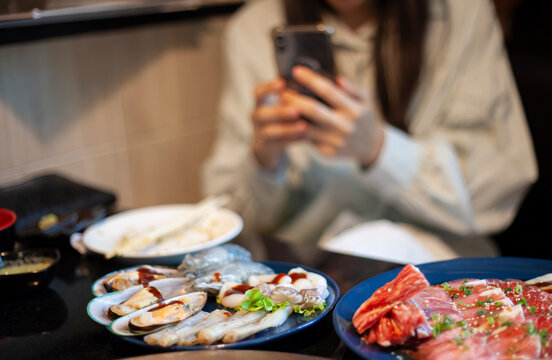 A woman taking food photos with a mobile phone in a restaurant