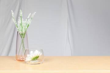A group of white flowers in a glass vase On a natural color wooden table against the background of white fabric