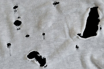 Gray white fabric with many holes. Texture of an old dirty ragged t shirt. Grunge damaged cloth on...