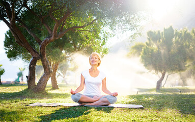 Yoga at park. Senior woman in lotus pose sitting on green grass. Concept of calm and meditation.