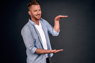 Horizontal shot of handsome Caucasian redhead man with bristle, shows height of something with both...