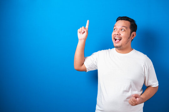 Photo image of Fat Asian man in white t-shirt looked happy thinking and looking up, having good idea. Half body portrait against blue background with copy space