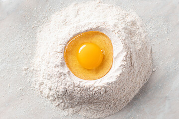 fresh egg in a heap of whole grain flour on a marble table. Basic baking ingredients. top view....