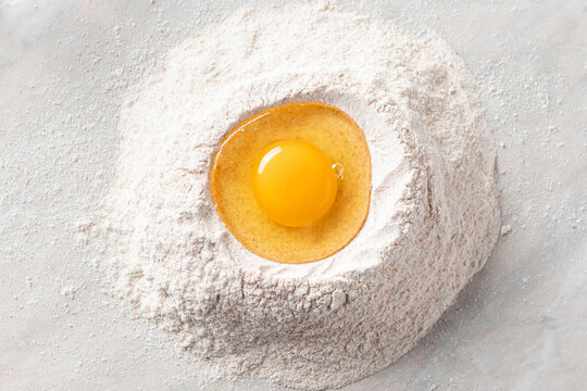 fresh egg in a heap of whole grain flour on a marble table. Basic baking ingredients. top view. horizontal image.
