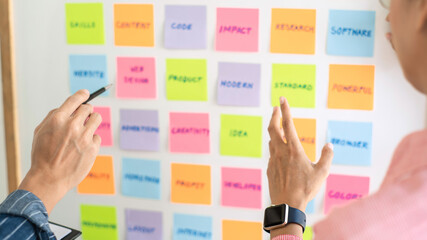 Business people meeting at office and use sticky notes on glass wall in office, diverse employees...