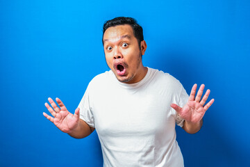 Naklejka premium Fat Asian man in white t-shirt shows funny shocked and surprise expression against blue background