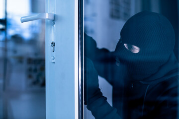 Robber in black balaclava cracking door with metal picklock - obrazy, fototapety, plakaty