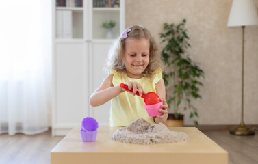 beautiful little girl sitting at the table and playing with kinetic sand and a shovel. development...