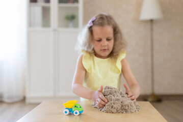 Cute little girl playing with kinetic sand and a toy car. kids games. horizontal image.