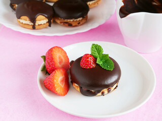 Sandwich cookies with chocolate glaze and strawberries on plate over pink background