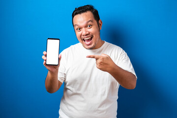 Pleased happy young fat asian guy in white t-shirt smiling to camera while holding smartphone pointing at cellphone screen