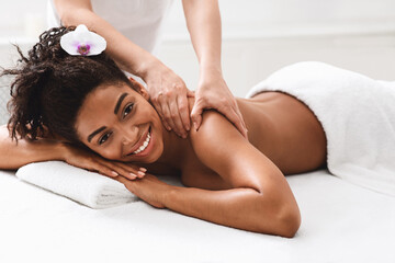 Happy african girl enjoying back massage at spa salon