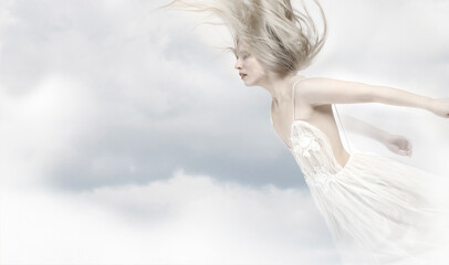 Young beautiful blonde girl flying in the clouds