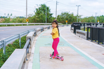 Naklejka premium Little child girl to ride scooter in outdoor sports ground on sunny summer day. Active leisure and outdoor sport for children.