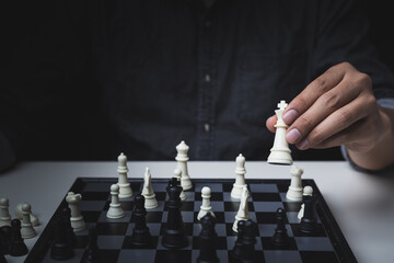 Close up view of the hand of a man with a white chess Wearing a black shirt On a black background, business competition concept