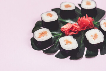 Japanese Food Sushi with Salmon and Ginger on With Tropical Leaves Monstera Pink Background Above Copy Space