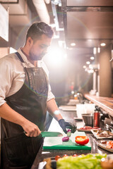 Serious bearded chef working at commercial kitchen and cutting red onion, lens flare