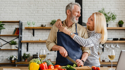 Happy senior couple cooking food with healthy fresh vegetables on kitchen at home. Concept of...