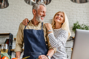 Happy middle aged couple having fun while making dinner at home kitchen