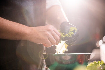 Close-up of unrecognizable chef tearing leaf vegetable and adding it into bowl, lens flare