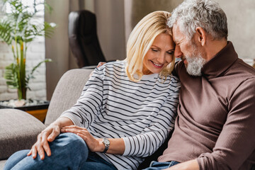 Joyful middle aged couple relaxing and hugging at home