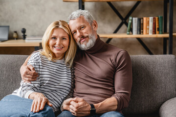 Middle aged couple relaxing on couch smiling at camera at home in living room