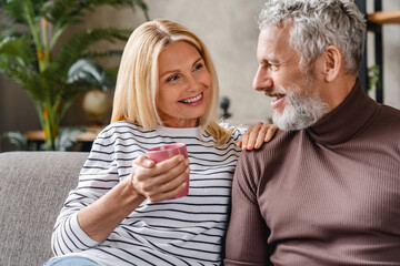 Smiling middle aged mature couple laughing and drinking coffee, having fun at home