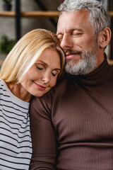 Fototapeta premium Vertical shot of middle aged couple in love hugging on sofa at home