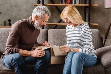 Middle aged couple opening parcel box at home. Delivery and shipping concept