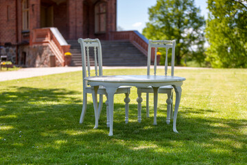 Outdoor white table and chairs on a green lawn near a brick building with a wide staircase.